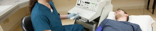 Two students in a sonography simulation, one in a bed and the other administering from a chair